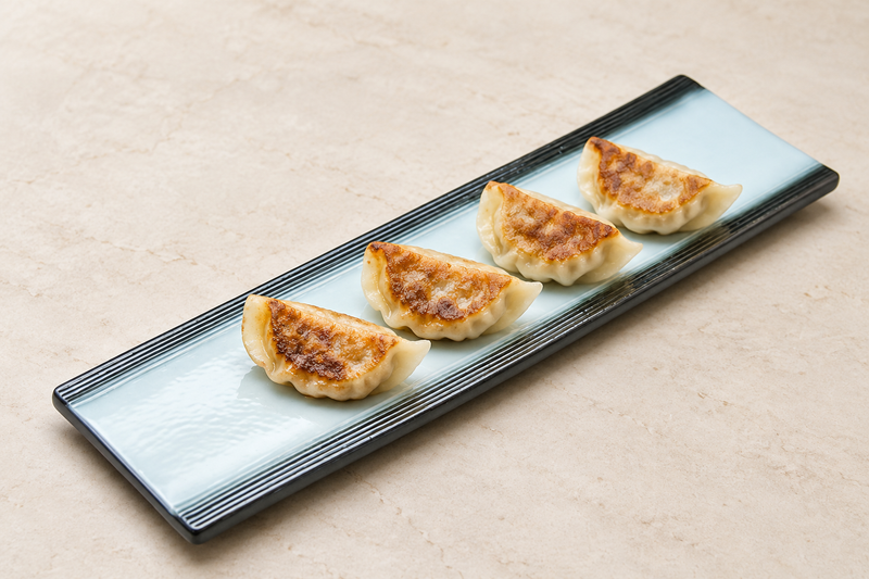 Light blue and black long porcelain platter holding a spaced row of four browned dumplings.