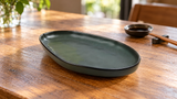 Empty RFR-13 dark green egg-shaped porcelain plate on a wooden table