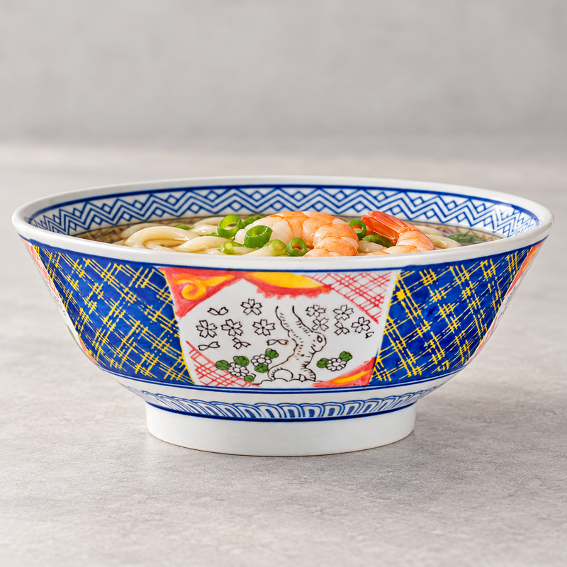 Patterned ceramic bowl holding noodles in broth with shrimp and green vegetables.