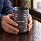 TCC20 dark speckled striped teacup held in both hands by a window