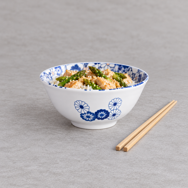 Blue floral ceramic bowl filled with rice and colorful toppings, with natural-tone chopsticks on a light gray tabletop.