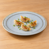 YG-7612BS round melamine plate with four gyoza on a wood table