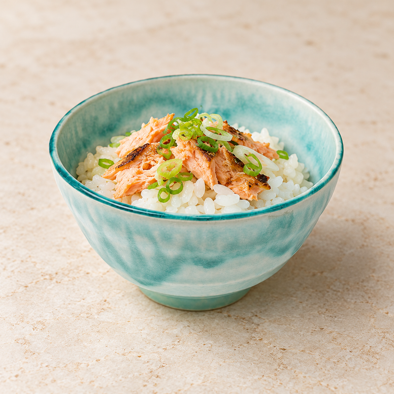Small turquoise ceramic bowl holding rice with flaked fish and sliced green garnish.