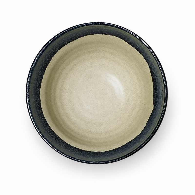 Overhead cream ceramic bowl with subtle circular interior bands and a broad dark speckled rim.