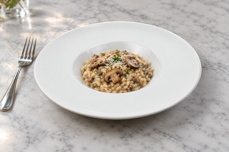 White wide-rim porcelain plate with a small mushroom risotto serving in the recessed center.