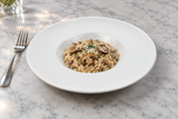 White wide-rim porcelain plate with a small mushroom risotto serving in the recessed center.