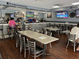 Clear-finish metal restaurant chair with black padded seat; restaurant setting with other furniture illustrative