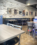 Clear-finish metal restaurant chair with black padded seat; restaurant setting with other furniture illustrative