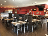 Clear-finish metal restaurant chair with black padded seat; restaurant setting with other furniture illustrative
