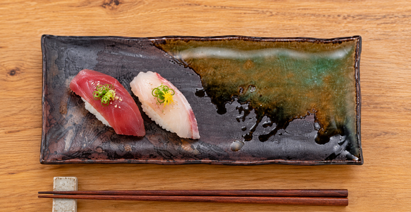 IM211-IK brown and green porcelain plate holding sushi on a wooden counter