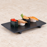 Black rectangular footed melamine plate holding sushi on stone