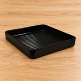 Black square melamine plate with ridged base on a tabletop