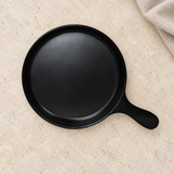 Black round melamine serving plate with handle on a tabletop