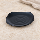 Black rounded-square melamine plate with subtle ripple detail on a tabletop