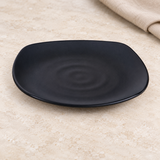 Black rounded-square melamine plate with subtle ripple detail on a tabletop