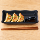 IT-Y301B black rectangular melamine plate with gyoza and dipping sauce in its integrated corner well