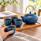 Blue textured tea set with one cup held and three cups on its tray