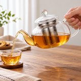 Clear glass teapot with steel infuser pouring tea into a small cup