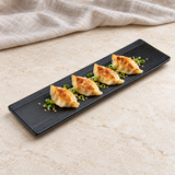 JX218-B long black ridged-edge platter with gyoza on a stone table