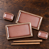 JX79-3 brown rectangular sushi set with two plates, two small dishes and two chopstick pairs, on a wooden table