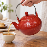 Red textured teapot with arched handle pouring tea