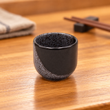KY8-NW black and gray speckled sake cup on a wooden table