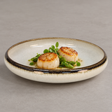 Ivory shallow ceramic plate with dark rim holding scallops