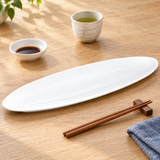 Long white oval platter with tea, sauce dish and chopsticks on light wood