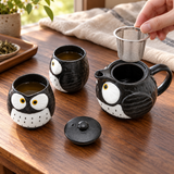 OWC4-B black and white owl teapot set with two cups in a open-pot infuser preparation setting. Tea, food and surrounding scene accessories are illustrative, not included.