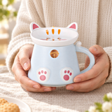 Pale-blue cat-paw mug with closed cat-ear lid cradled in hands