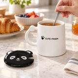 PC53-2 white panda mug viewed from the reverse while tea is stirred with its black lid alongside