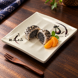 508-E Eggplant-pattern melamine plate — Small dessert selection of one black sesame mochi cut in half with mandarin segments, dark wooden tabletop and dessert fork outside plate