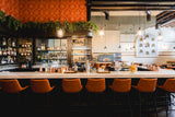 Pumpkin Upholstered Restaurant Barstool with Wood-Grain Metal Frame in a restaurant setting; other furniture is illustrative