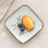 Square floral plate with a madeleine and blueberries on a stone tabletop