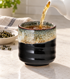 Black and speckled cream teacup being filled with tea