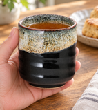 Black and speckled cream teacup held during a tea break