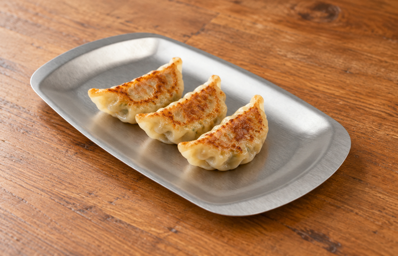 Silver rectangular plate with three dumplings on a wooden table