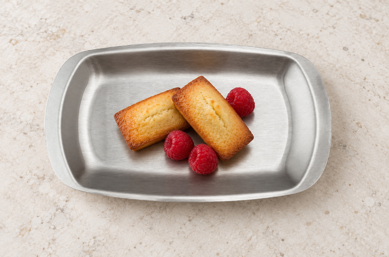 Silver rectangular plate with small cakes and raspberries on a stone table