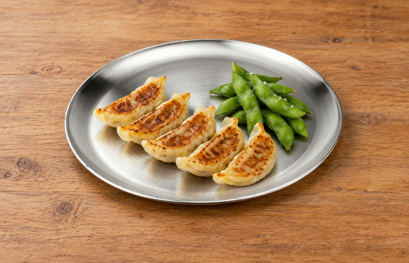 Round silver plate with gyoza and edamame on a wooden table