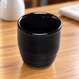 A1888-B black ceramic sake cup on a wooden restaurant table