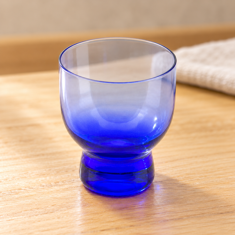 Blue JN24-B glass sake cup with a short foot on a wooden table
