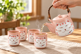 Pink smiling-cat teapot pouring tea into one of four cups