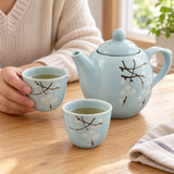 TPS2-722 sky-blue white-blossom teapot with two cups in a cup-serving setting. Tea and surrounding scene accessories are illustrative, not included.