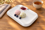 White rectangular porcelain plate with two mochi, blueberries and berry coulis in the raised square saucer area.