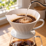 White HARIO V60 size 01 tabbed paper filter in a coffee-brewing setting. Dripper, server, coffee and surrounding scene accessories are illustrative, not included.