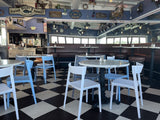 White open-back plastic restaurant chair; restaurant setting, other furniture illustrative