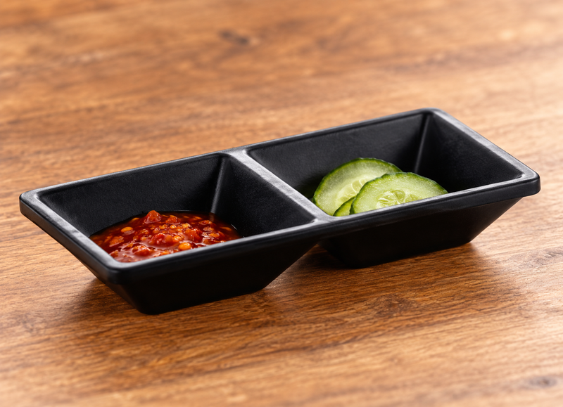Matte black two-compartment sauce dish with chili sauce and cucumber pickles