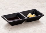 Matte black two-compartment sauce dish with soy sauce and pickled ginger