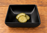Matte black square sauce dish with three cucumber pickle slices