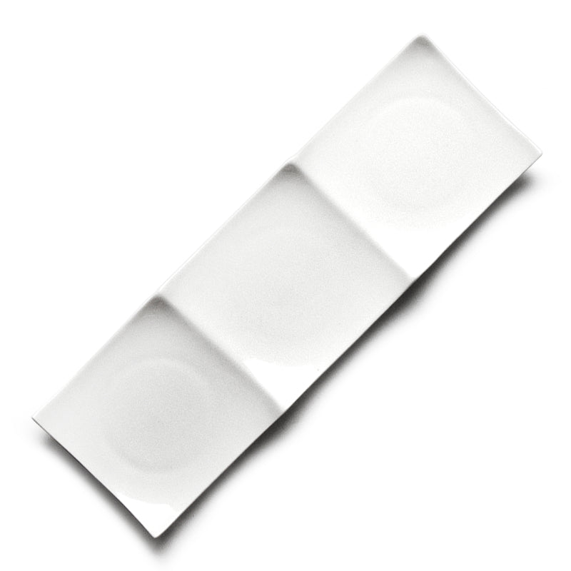 Overhead view of a long white ceramic rectangular plate with three shallow sections and curved raised edges.